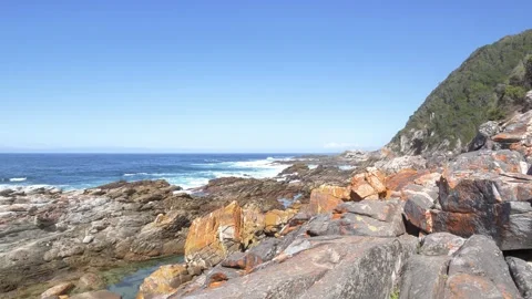 Rugged coastal cliffs meet the ocean waves under a clear blue sky. Vidéo 333028802