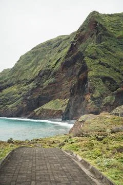 Rugged coastal landscape with a paved path leading to a hidden bay and maje.. Stock Photos