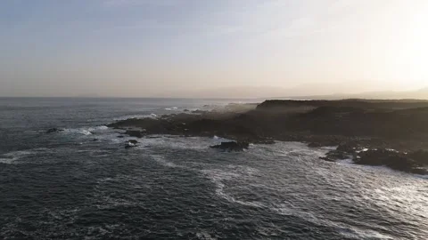 Rugged Dark Coastline Meets Rolling Ocean Waves in Warm Low Sunlight Stock Footage 344952758