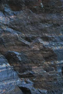 Rugged dark stone surface with bluish grey tones and brown mineral streaks Stock Photos
