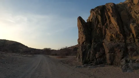 A Rugged Desert Road Winds Beneath Towering Rocky Cliffs Vídeo Stock 320502203