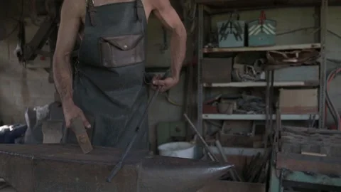 A rugged forger, leather apron-clad, forges iron with a hammer and anvil. Stock Footage 253201242