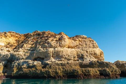 Rugged golden limestone cliffs tower over the calm emerald Atlantic waters .. Stock Photos