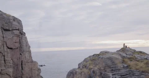 A rugged, grey cliff overlooks calm water under an overcast sky. A solitary Stock Footage 337512261