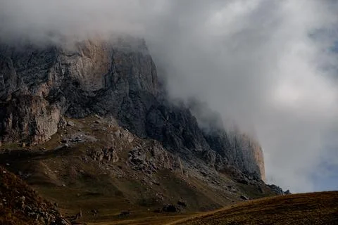 A rugged mountain landscape with steep cliffs and a cloudy sky. The terrain is Stock Photos