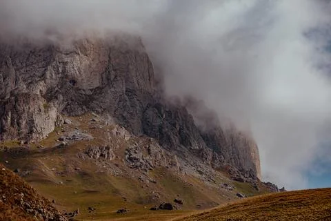 A rugged mountain landscape with steep cliffs and a cloudy sky. The terrain is Stock Photos