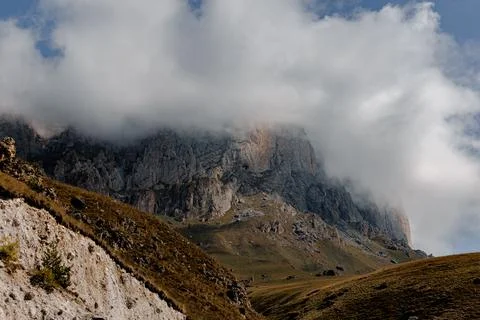 A rugged mountain landscape with steep cliffs and a cloudy sky. The terrain is Stock Photos