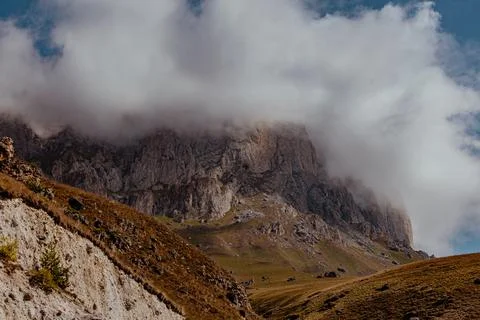A rugged mountain landscape with steep cliffs and a cloudy sky. The terrain is Stock Photos