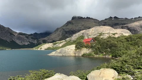 Rugged mountain peaks with a red-roofed cabin by a blue lake Stock Footage 310611217