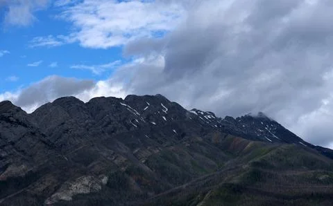 Rugged Mountain Range and Snow Patches Under Shifting Storm Clouds Stock Photos