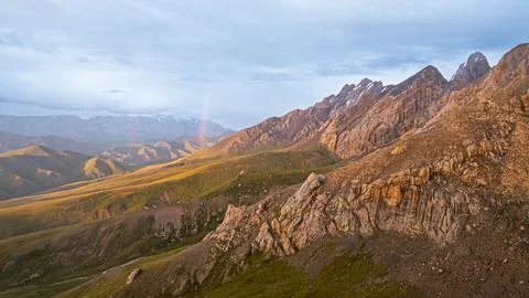 Rugged mountain range with golden light and distant rainbow Stock Photos