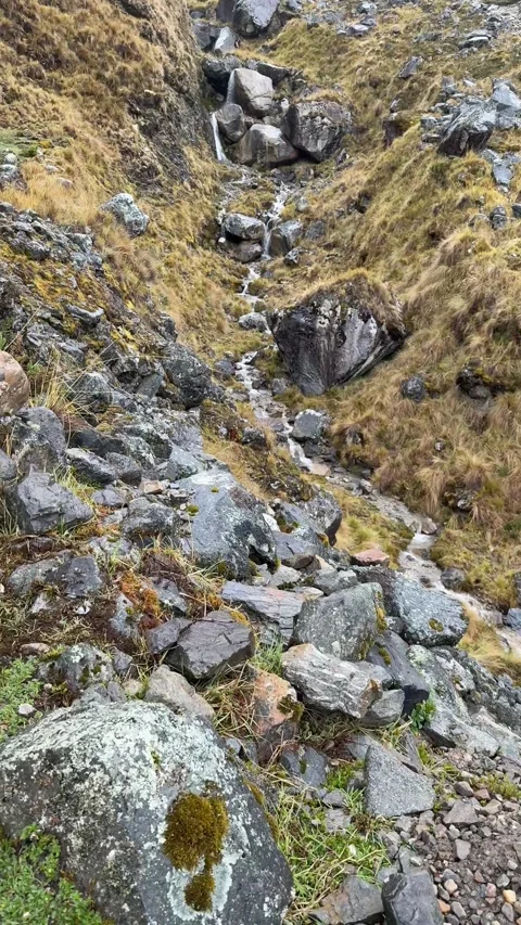 Rugged mountain trail through rocky slopes with stream and hikers in distance. Stock Footage 322114232