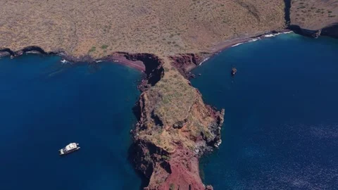 Rugged red volcanic cliffs bordering deep blue Pacific waters, yacht navigating 스톡 동영상 308419739