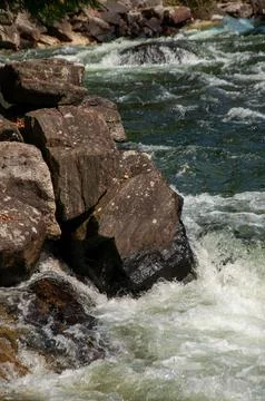 Rugged River Rapids Flowing Around Large Rocks on a Sunny Day Foto stock