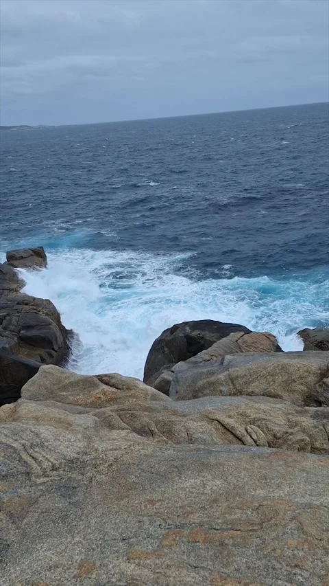 Rugged rocky coast with ocean waves crashing on granite rocks under cloudy sk Video stock 335654142