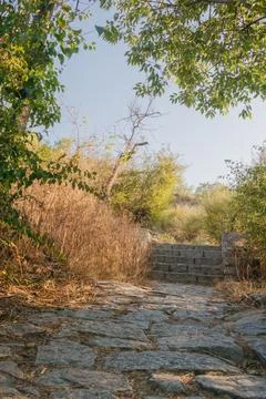 Rugged stone path and steps winding uphill through dry grass and scrub unde.. Stock Photos