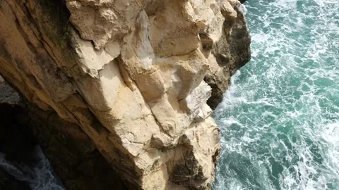 Rugged vertical cliff face close up stone texture waves breaking at its base Stock Footage 341800246