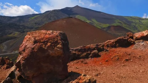Rugged volcanic landscape with large, rust-colored rock, and cinder cone  Vidéo 314886211