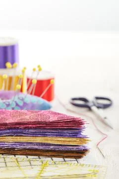 Ruler, cutting mat, stack of multi-colored pieces of fabric, pincushion, spool Stock-Fotos