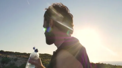 Runner arrives on top of a cliff on an island in front of the ocean and drinks Stock Footage 80233135