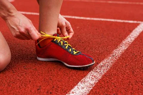 A runner bending down to tie their sneakers on the racing track before the .. Stock Photos