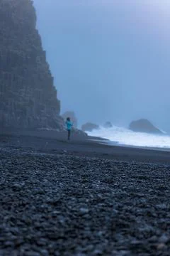 Runner in Blue Jacket on Black Sand Beach Iceland with Basalt Cliffs Foto stock