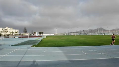 Runner Builds Speed Along Outdoor Athletics Track Beside Grass Field Video stock 345454806