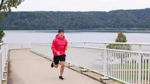 Runner in colored clothes runs across bridge in morning and runs out of frame 스톡 동영상 253826120
