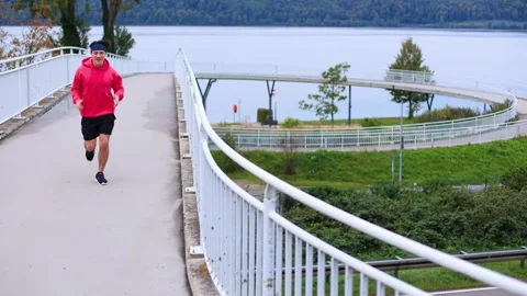 Runner in colored clothes runs across bridge in morning and runs out of frame Vidéo 253826254
