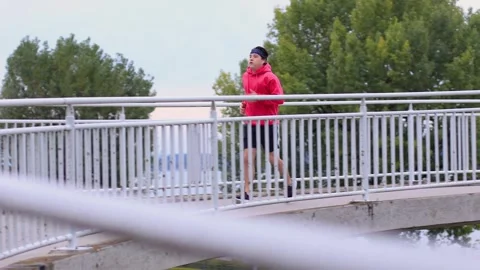 Runner in colored clothes runs across bridge in morning and runs out of frame 스톡 동영상 253826428