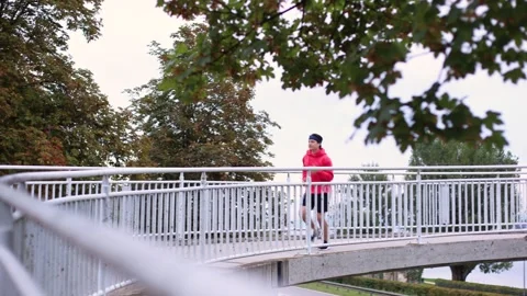 Runner in colored clothes runs across bridge in morning and runs out of frame 스톡 동영상 259489345