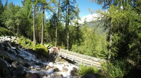 Runner crossing rapid stream above the wood bridge in mountains Stock Footage 53925538