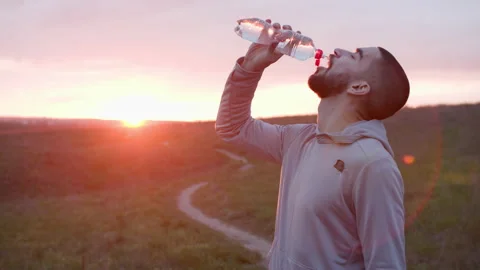 Runner drinking water after workout in field Stock Footage 153565695