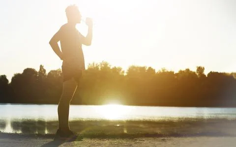 Runner drinks water while jogging in the park. Stock Photos