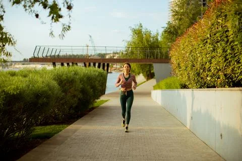 Runner enjoys jogging along the river pathway in a city park during afternoon 写真素材