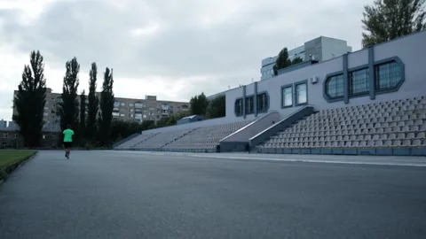 A runner in a green jacket runs in an old abandoned stadium Stock Footage 163915682