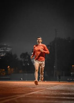 Runner heading towards the camera on a red track under a night sky 写真素材