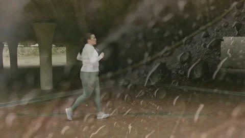 Runner jogging from left underpass entering frame and passing columns with rain Stock Footage 334202683
