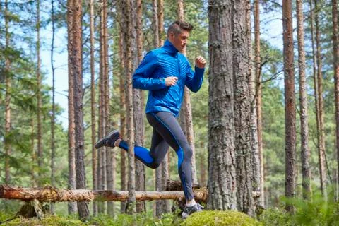 Runner jumping over fallen log on trail in woods Stock Photos