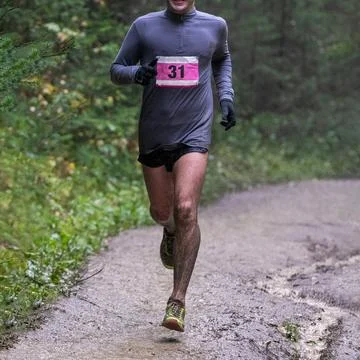 Runner in numbered bib running muddy forest trail during marathon Stock Photos