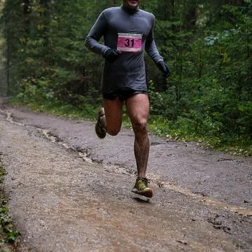 Runner in numbered bib running muddy forest trail during marathon race Stock Photos