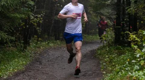 Runner in numbered race bib running muddy forest trail Stock Photos