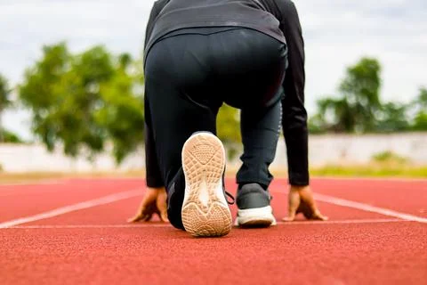 Runner poised at starting blocks on a red track, ready for race, athletic foc Stock Photos