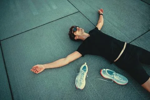 Runner recovering on pavement after intense workout with his shoes removed Stock Photos