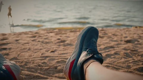 Runner resting on sandy beach after running along the river bank at sunset Stock Footage 292868743