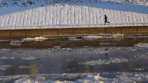 Runner running in cold weather next to the icy river. Fit athlete jogging Stock Footage 147503347