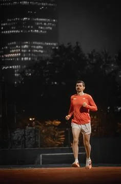 Runner running towards the camera on a red track at night 写真素材