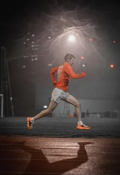 Runner in side view with a long shadow on a damp track at night Фото