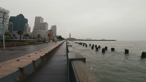 Runner on sidewalk next to waterfront in downtown San Francisco on a rainy day Stock Footage 273809948