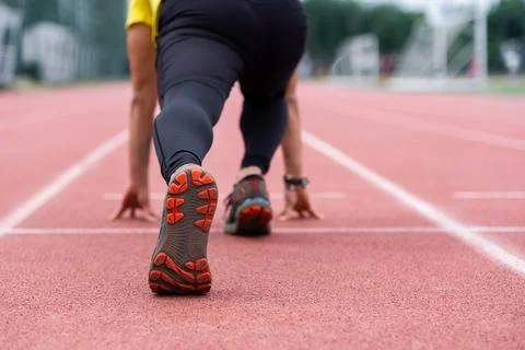 Runner standing in low start position ready to run along red rubberized track on Stock Photos